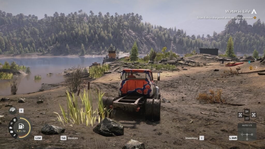 A truck crosses a rocky beach beside a forest