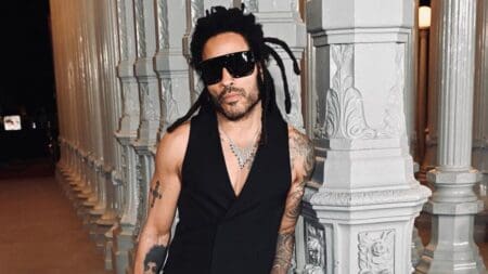 Lenny Kravitz leans against a pillar while wearing an all-black outfit.