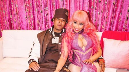 Nicki Minaj in a pink outfit sits on a couch with her husband Kenneth Petty.