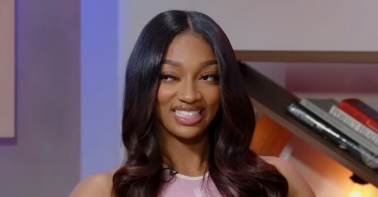 Angel Reese sitting down in a pink dress smiling.