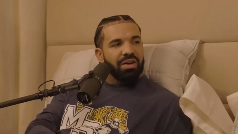 Drake sitting on bed in front of a microphone.