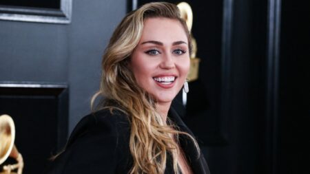 Miley Cyrus smiles on red carpet.