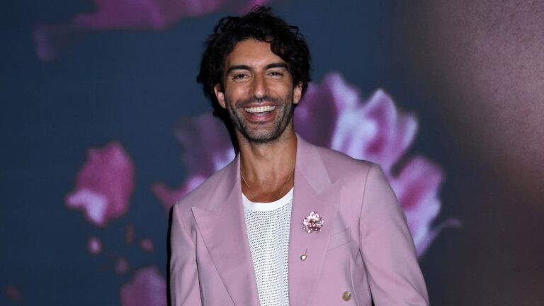 Justin Baldoni in a pink suit posing on the red carpet for a photo.