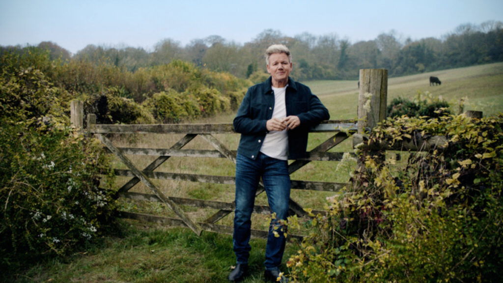 Gordon Ramsay leans against a farmyard fence in an ad for his Hay Day crossover