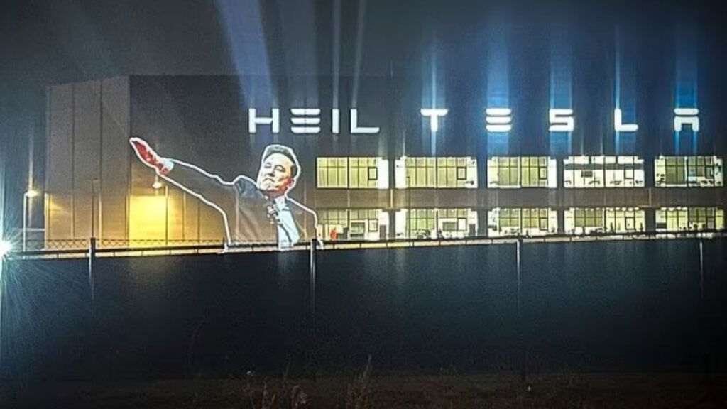 Protesters project an image of Elon Musk giving the Nazi salute, along with the word "Heil" on the side of a Tesla factory