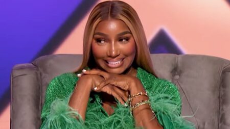 NeNe Leakes in a green outfit sitting in a chair smiling.