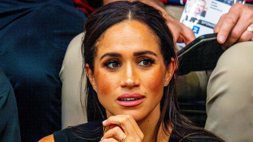 Meghan Markle rocks black top and ruffled middle-parted hair on the audience stand at an event.