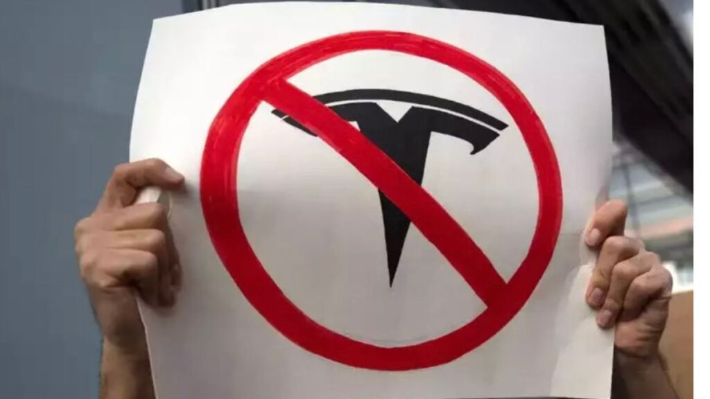 two hsnds holding a tesla protest sign