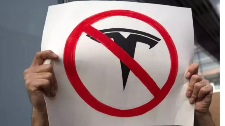 two hsnds holding a tesla protest sign